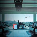 An empty modern airport departure lounge with seating and plane taking off in the background